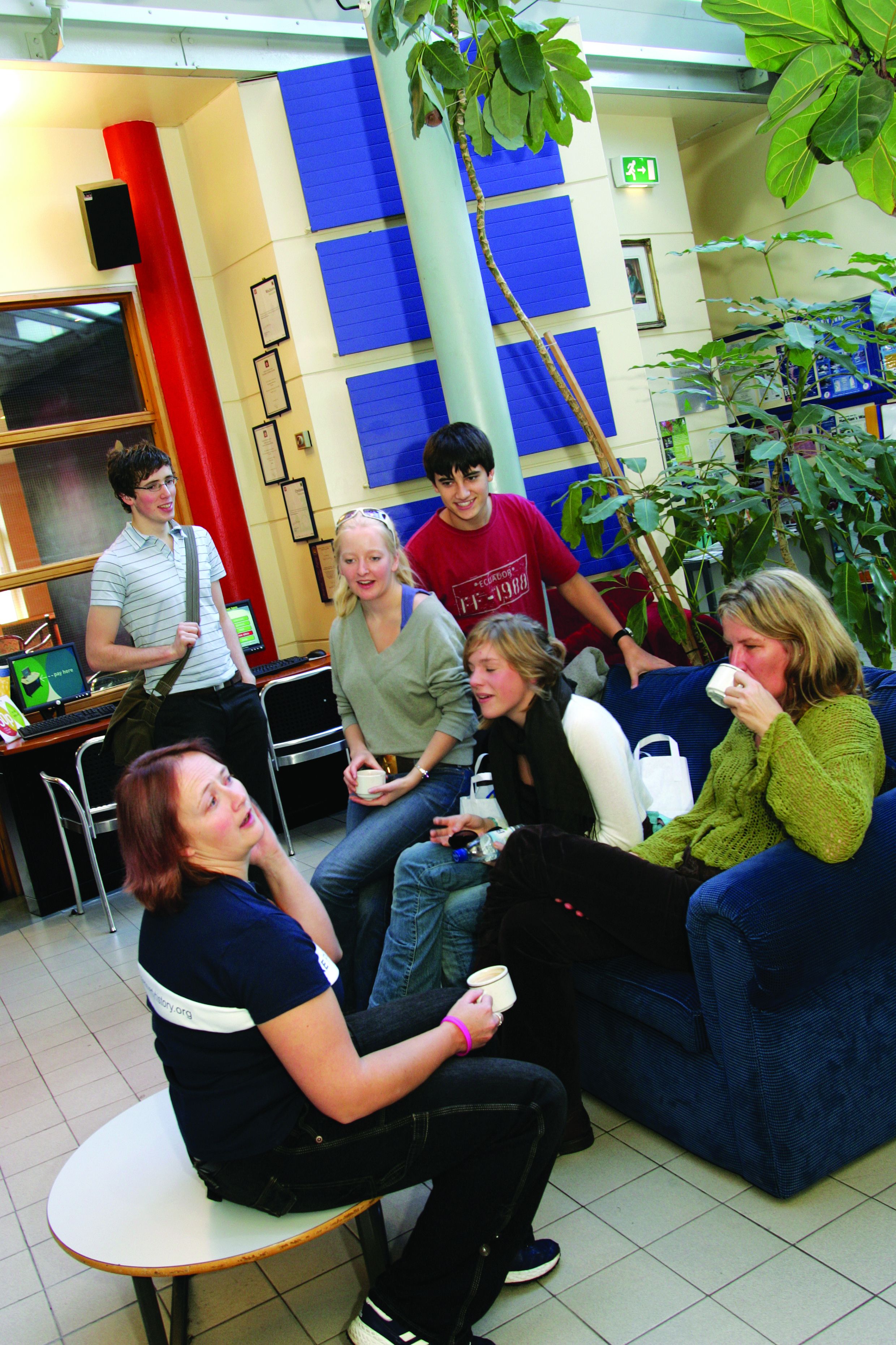 A group of people sitting on a blue couch and a table in a room with a red pillar and framed certificates on the wall.