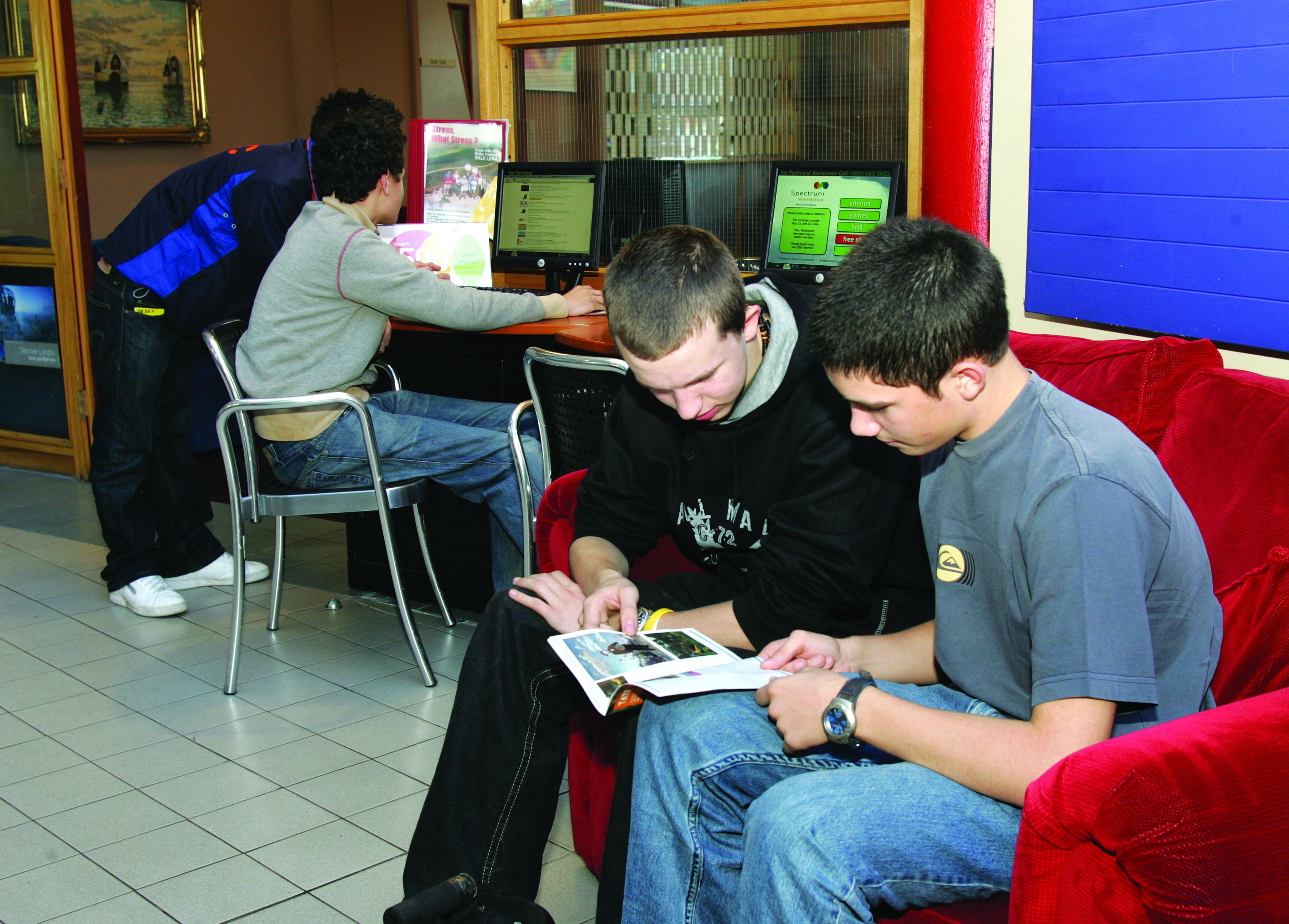 A group of people in a public space with computers and a poster on the wall.
