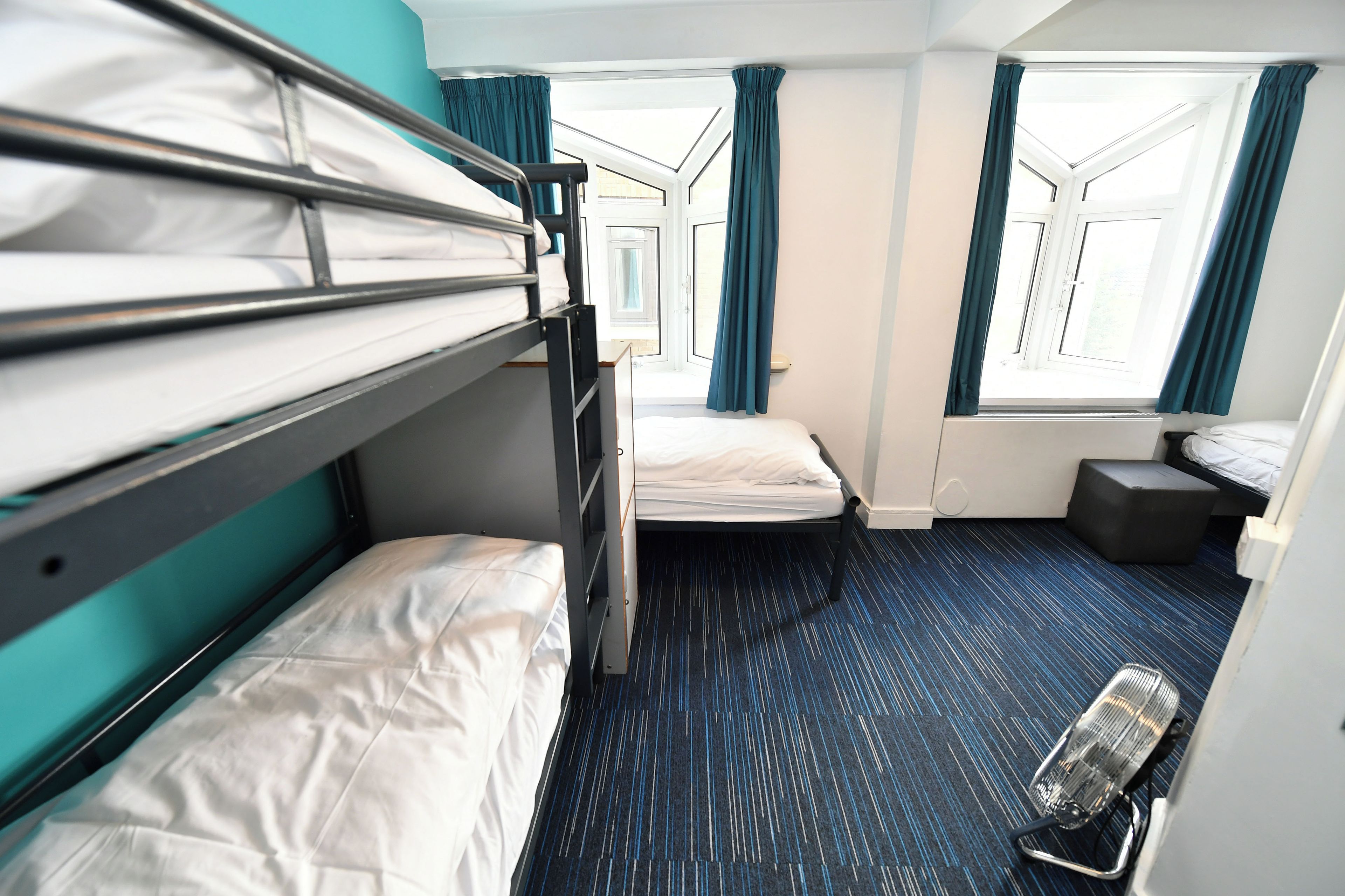 A hotel room with bunk beds, a small desk, a chair, and a window with curtains.