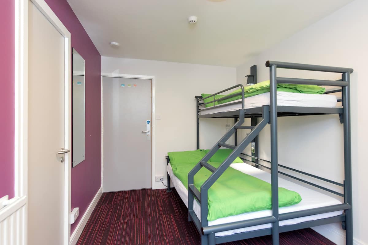 A small room with a bunk bed, a door, and a red carpeted floor.
