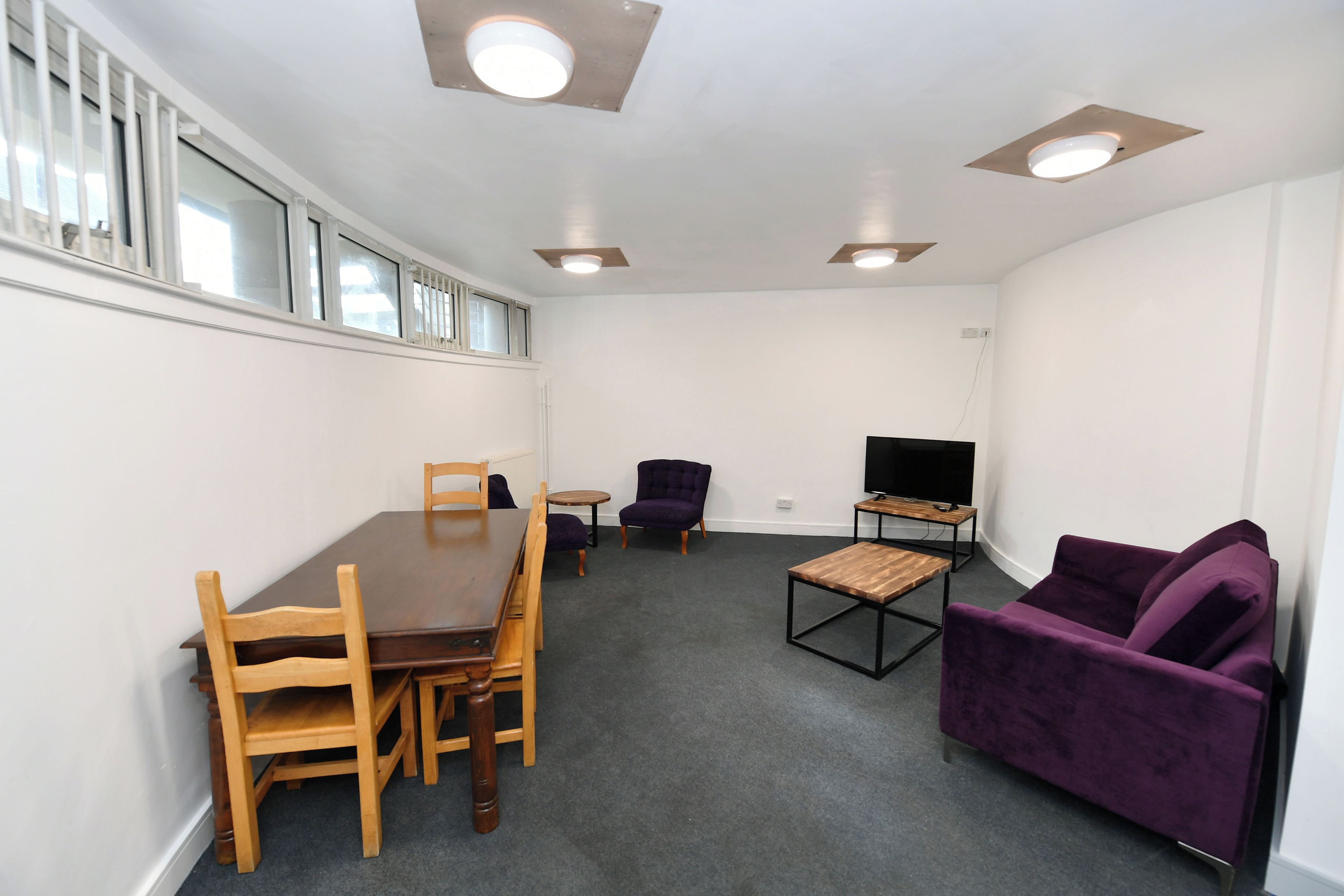 Ein Zimmer mit Esstisch, Stühlen, einer Couch, einem Fernseher und Einbauleuchten.