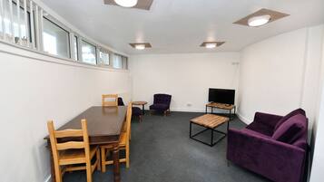 Ein Zimmer mit Esstisch, Stühlen, einer Couch, einem Fernseher und Einbauleuchten.