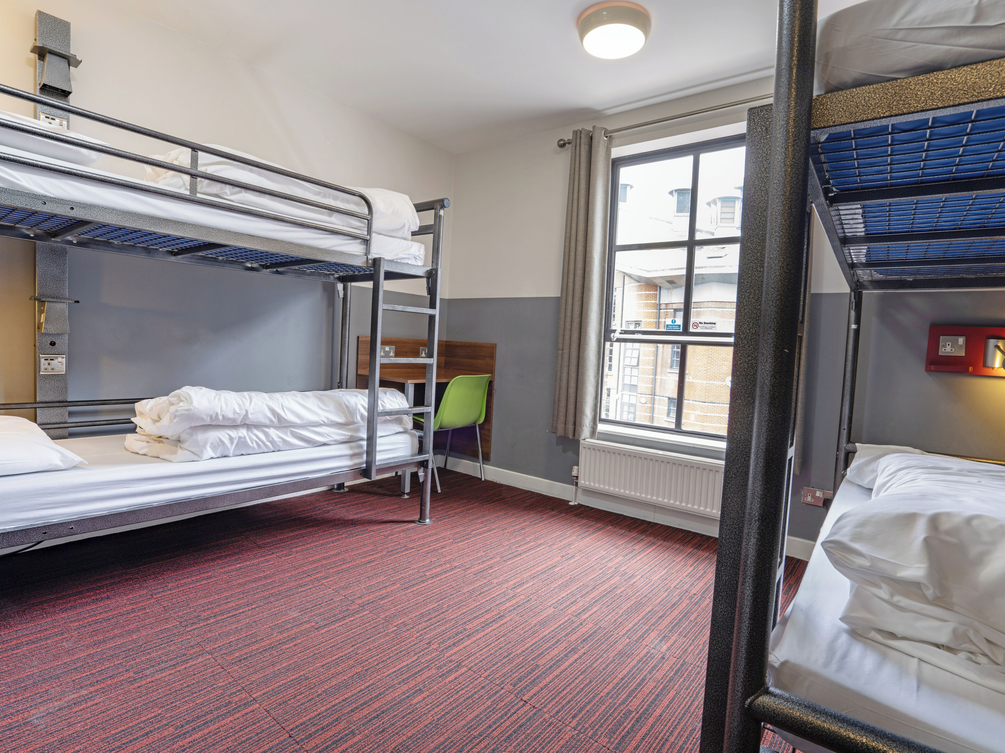 A bunk bed room with a desk and chair, a radiator, and a window with curtains.