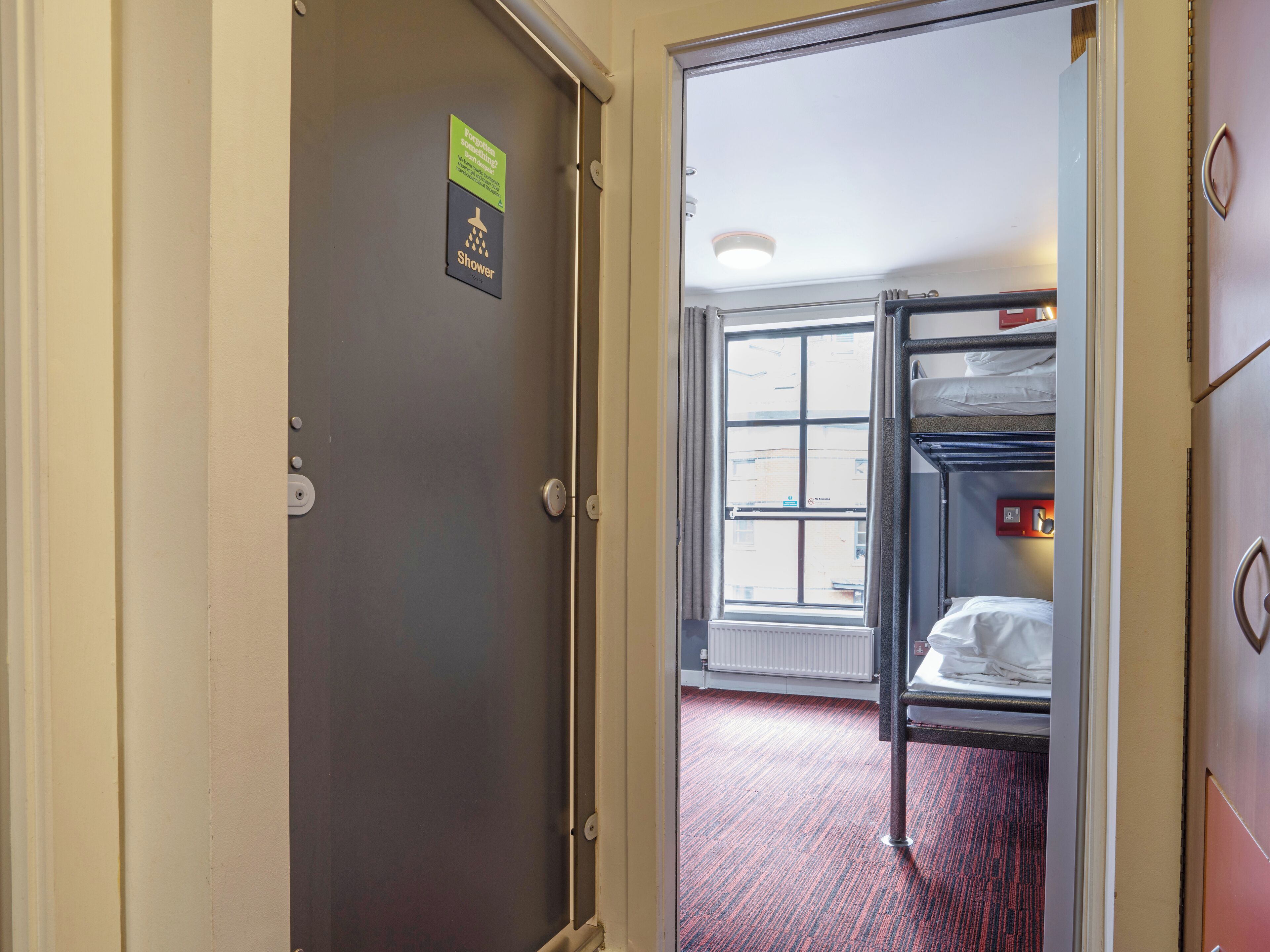 A hotel room with a bunk bed, a shower sign, and a window with a view.