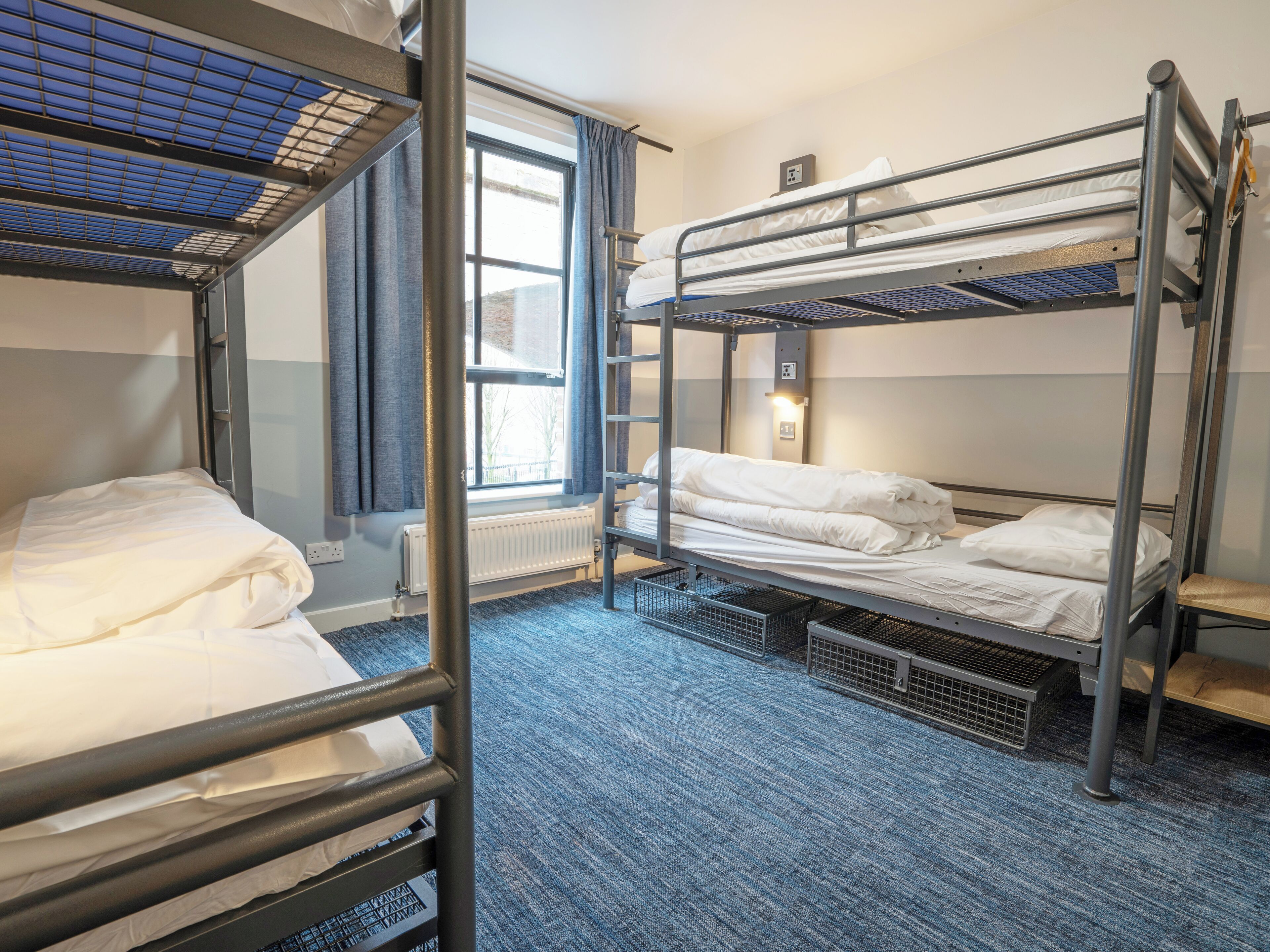 A bunk bed room with a window, a radiator, and a power outlet on the wall.