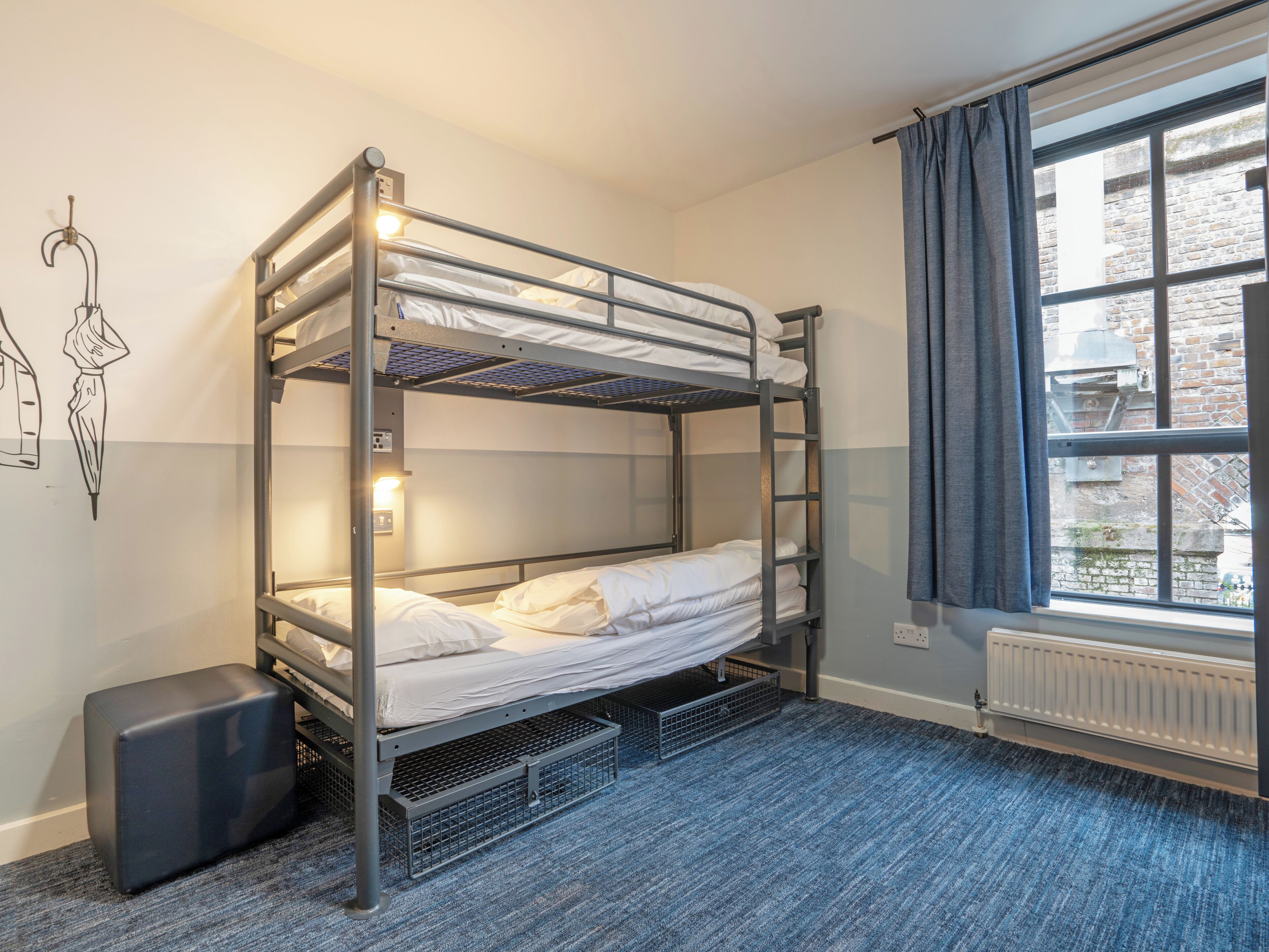 A bunk bed room with a window, a radiator, and a small stool.