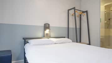 Habitación de hotel con cama, mesita de noche, armario y zona de ducha.