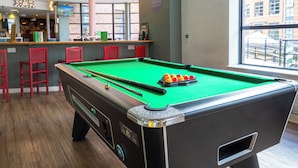 A pool table with balls, red chairs, and a bar area with a TV. - YHA Manchester - Hostel (Manchester)