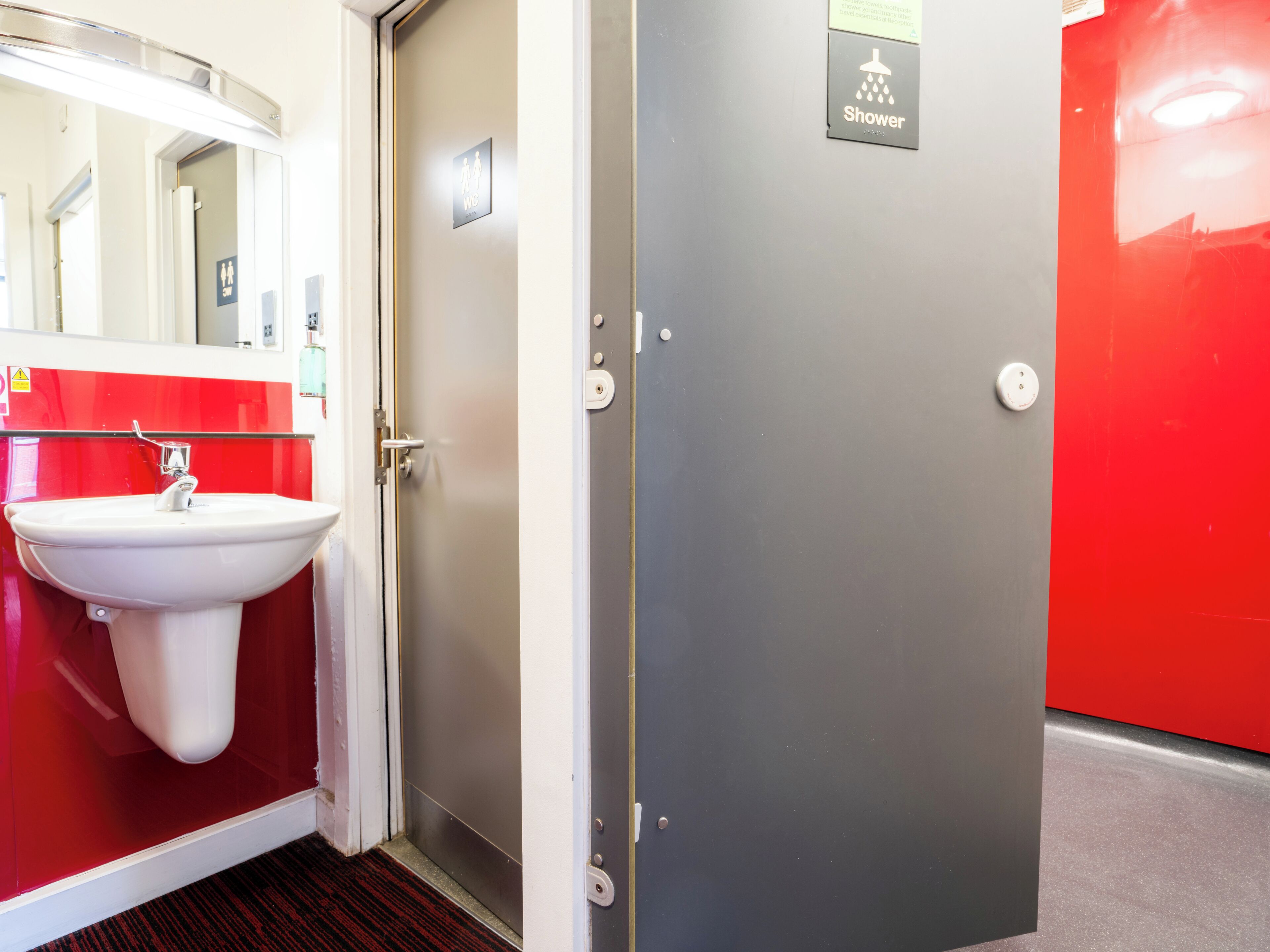 A bathroom with a sink, a shower sign, and a red wall.