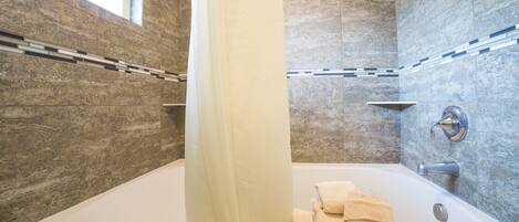 A modern bathroom with a bathtub, a window, and a towel rack.