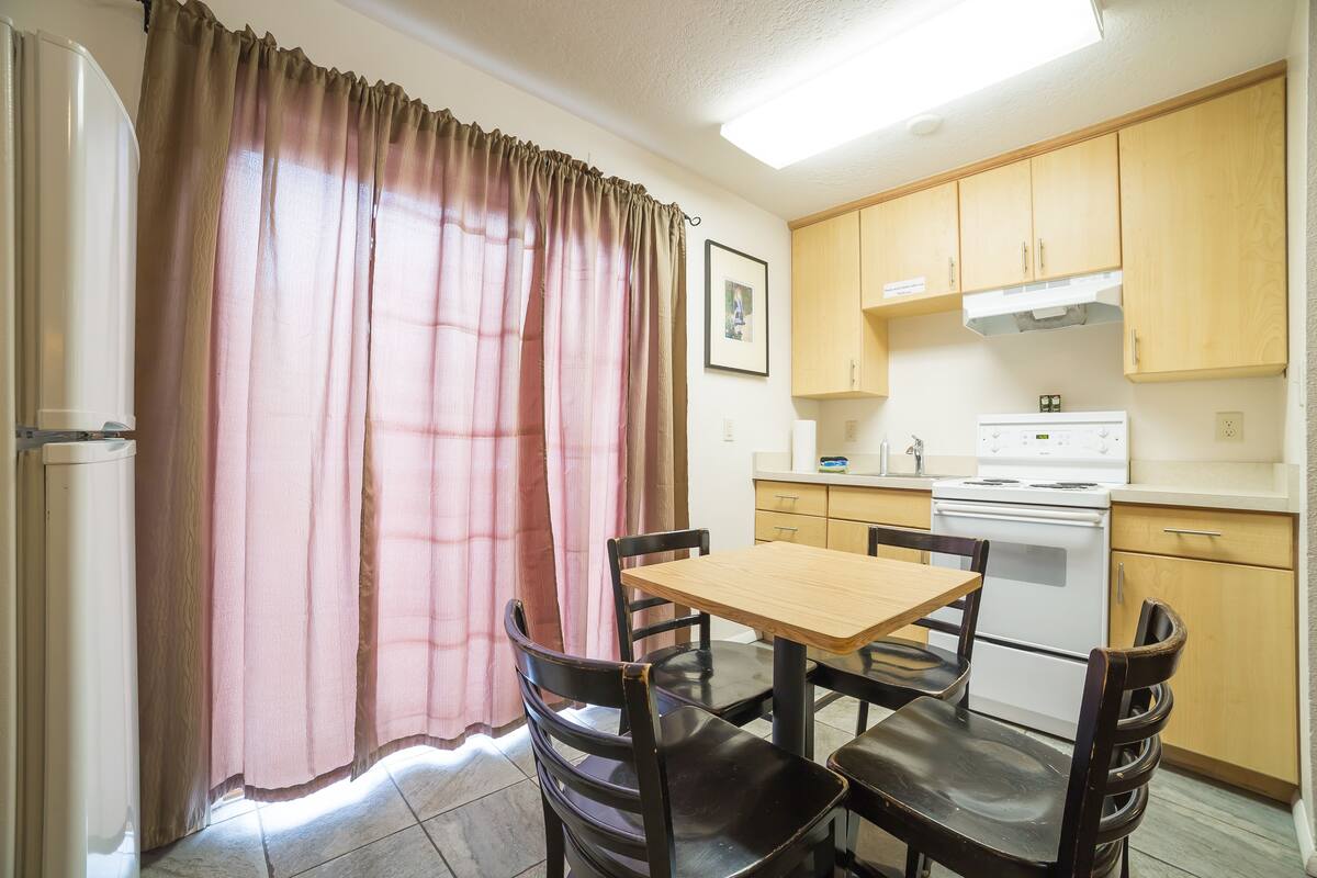 A compact kitchen with a dining table and chairs, a refrigerator, and wooden cabinets.