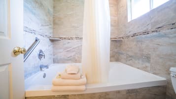 A modern bathroom with a bathtub, a shower area, and a toilet. There are towels stacked on the edge of the bathtub.