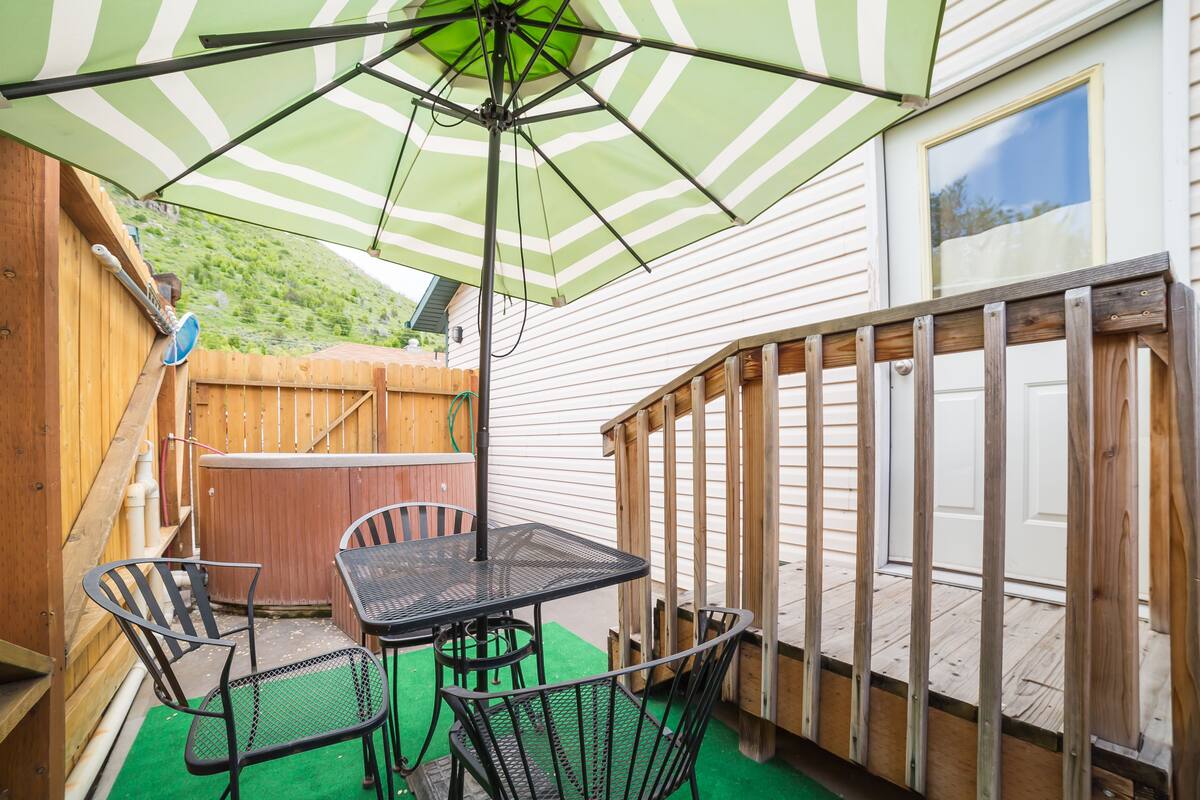 A patio with a green and white striped umbrella, a table, and two chairs.