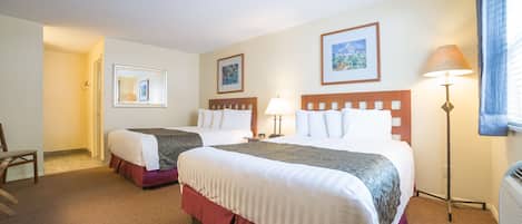 A hotel room with two beds, a chair, a lamp, and framed pictures on the walls.