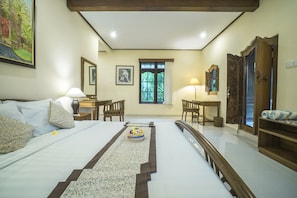 A hotel room with a bed, a desk, a chair, a window with a view of greenery, and a door. - Nyoman Sandi Guest House (Ubud)
