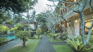 A courtyard with a paved walkway, palm trees, and a pool. - Nyoman Sandi Guest House (Ubud)