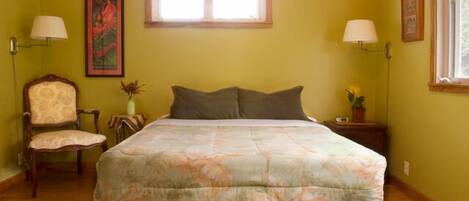 A bedroom with a bed, two bedside lamps, a chair, a window, and a painting on the wall.
