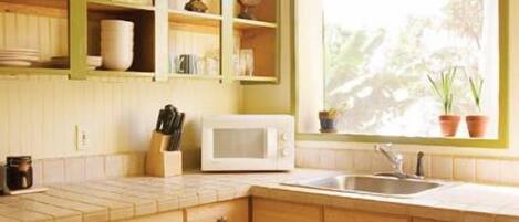 A kitchen with wooden cabinets, a white microwave, and a window with plants.
