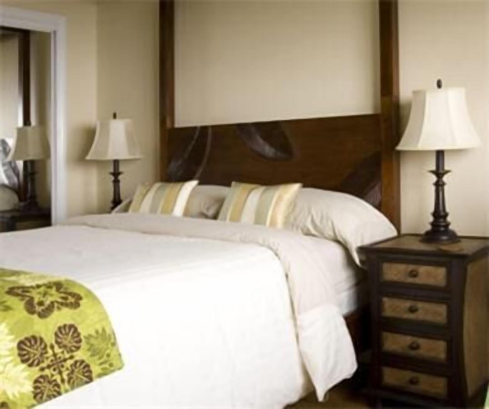 A hotel room with a bed, a nightstand with a lamp, and a dresser with drawers.