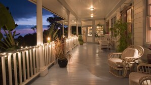 A covered porch with white railings, wicker furniture, and potted plants. - Ka'awaloa Plantation Bed & Breakfast (Captain Cook)