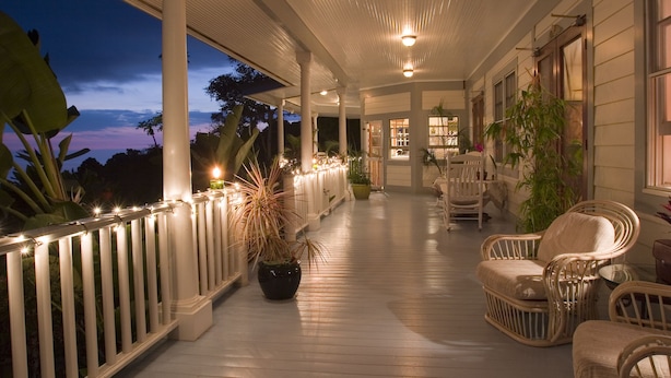 Une véranda couverte avec des balustrades blanches, des meubles en osier et des plantes en pot.