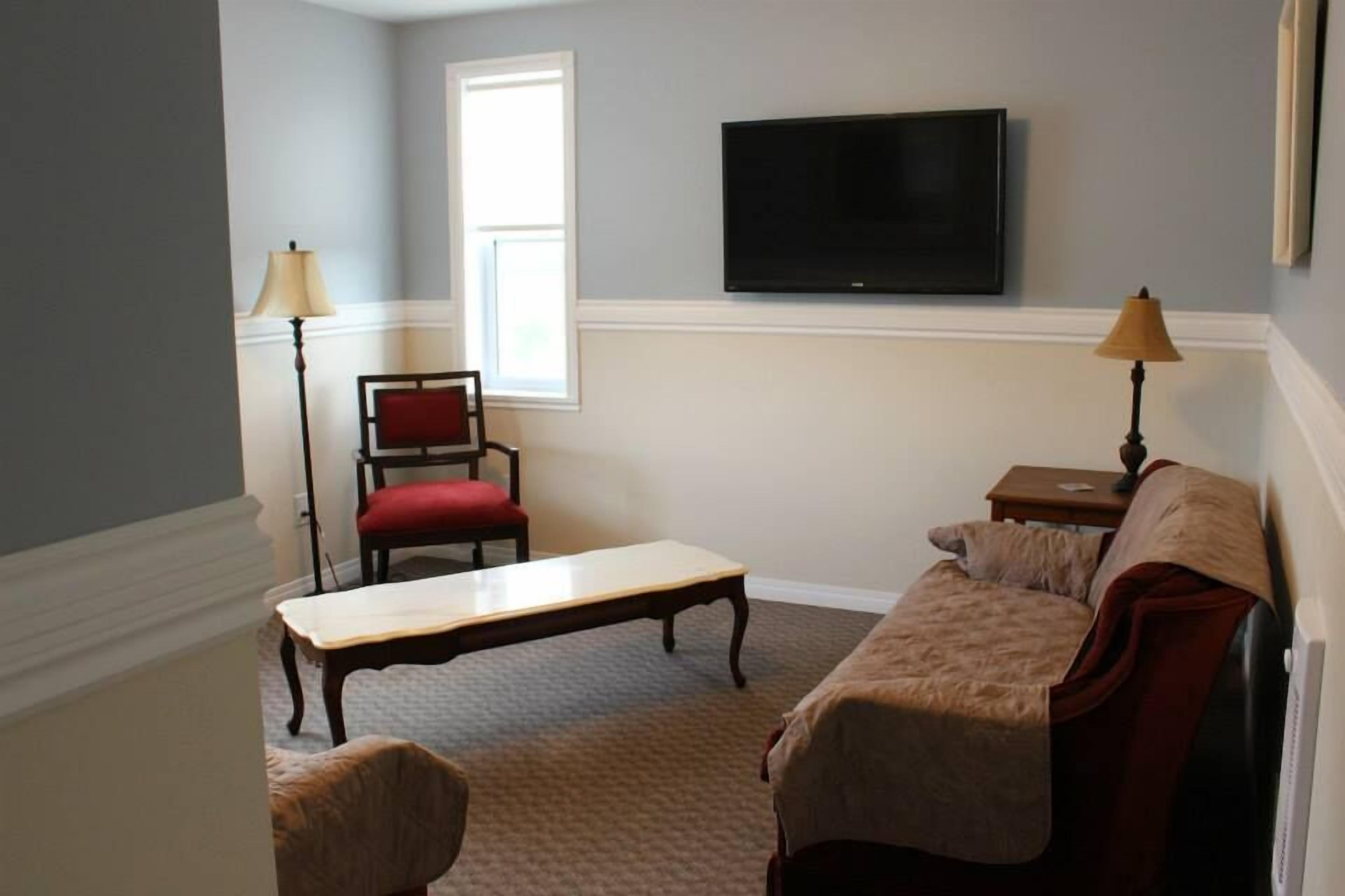 A living room with a television mounted on the wall, a red chair, a wooden table, and a sofa.