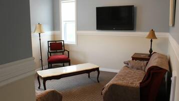 A living room with a television mounted on the wall, a red chair, a wooden table, and a sofa.