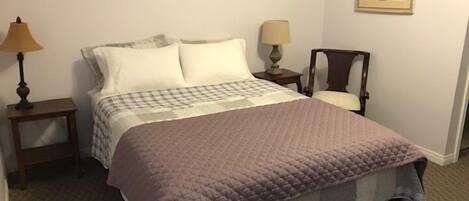A neatly made bed with a checkered bedspread and a purple quilt, a bedside lamp, a small table, and a chair.