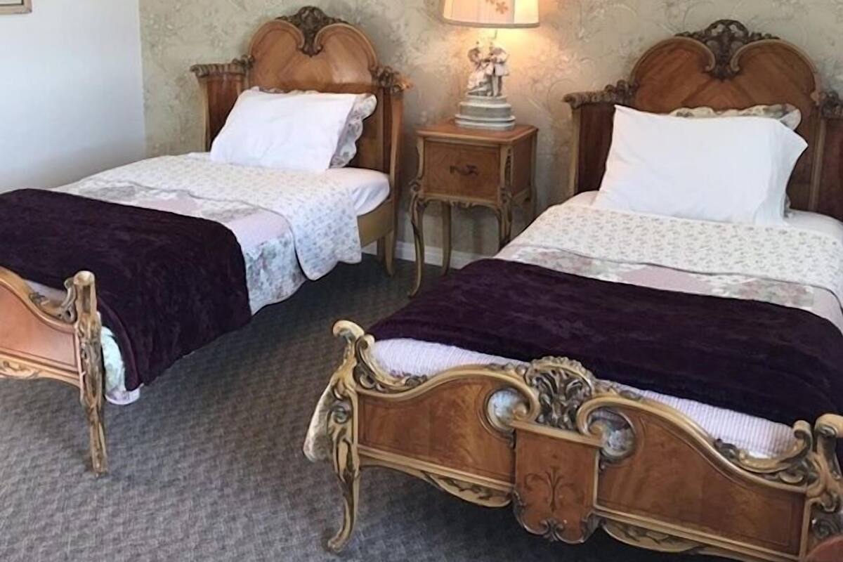 A room with two ornate wooden beds, a nightstand with a lamp, and a floral wallpaper.