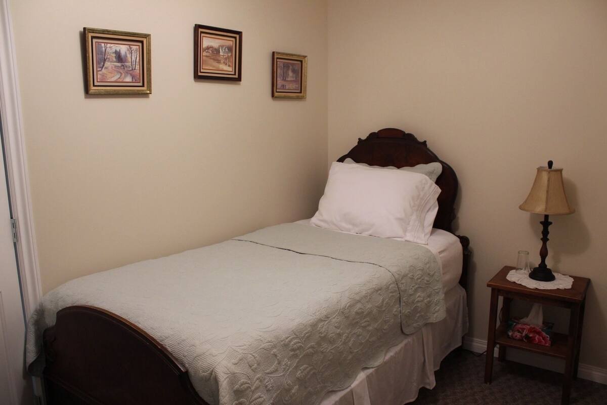 A single bed with a white comforter and a wooden headboard, a bedside table with a lamp, and three framed pictures on the wall.