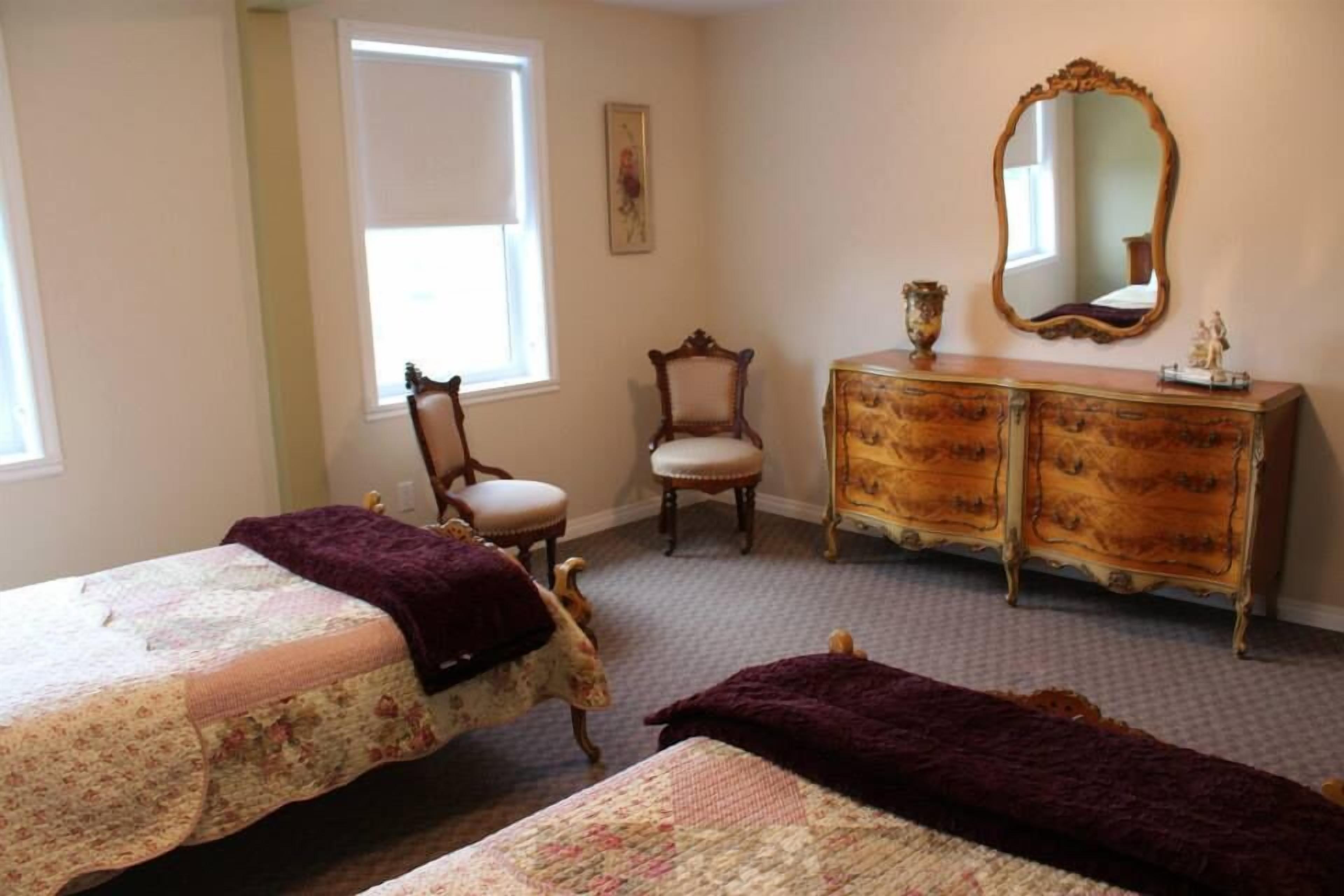 A bedroom with two beds, a dresser, a chair, and a large mirror.