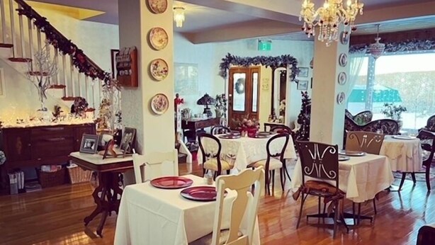 A dining area with tables set for a meal, a staircase with a floral garland, and a chandelier. - Honeycomb Bed & Breakfast (Onanole)
