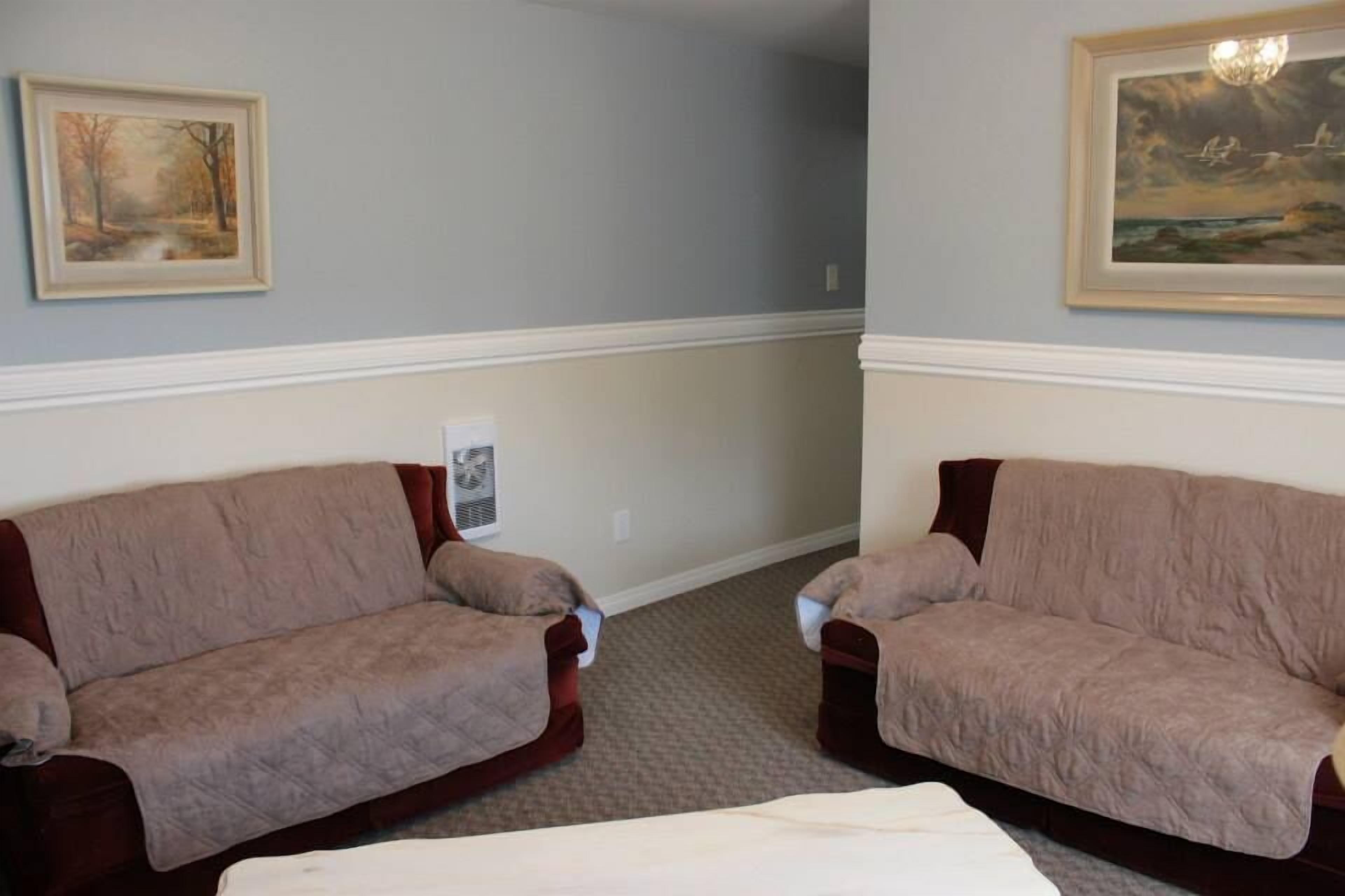 A room with two couches, a white bed, and a framed painting on the wall.
