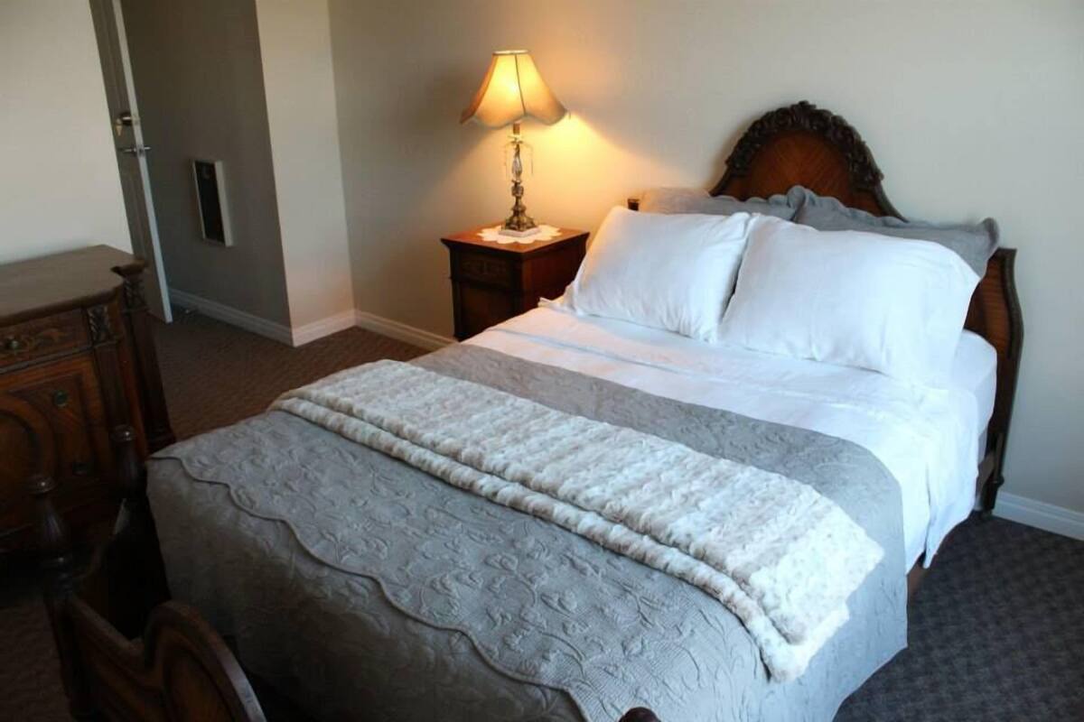 A neatly made bed with a white comforter and pillows, a bedside lamp, and a wooden nightstand.