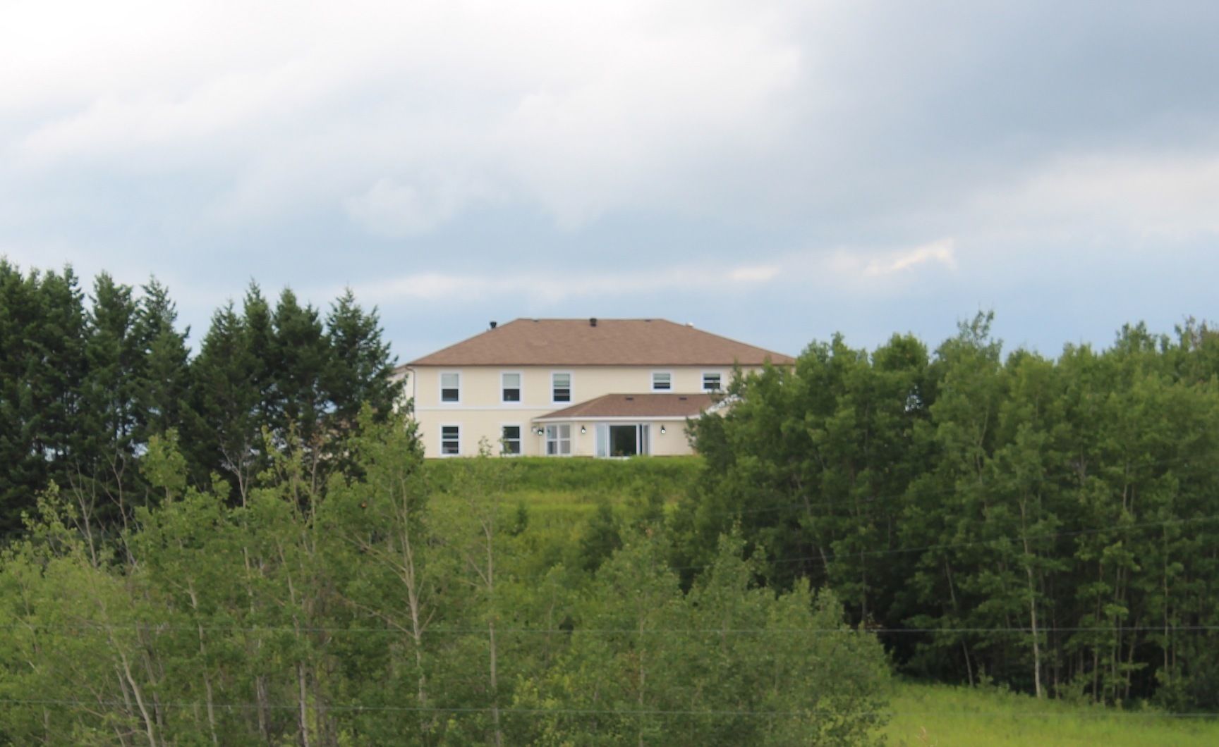 A two-story building with a brown roof, surrounded by dense green trees.