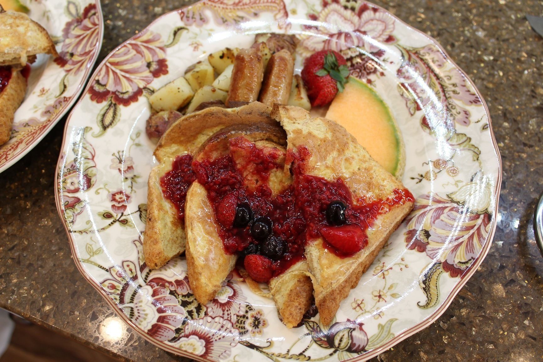 A plate of French toast with berries and a slice of avocado on a floral-patterned plate.