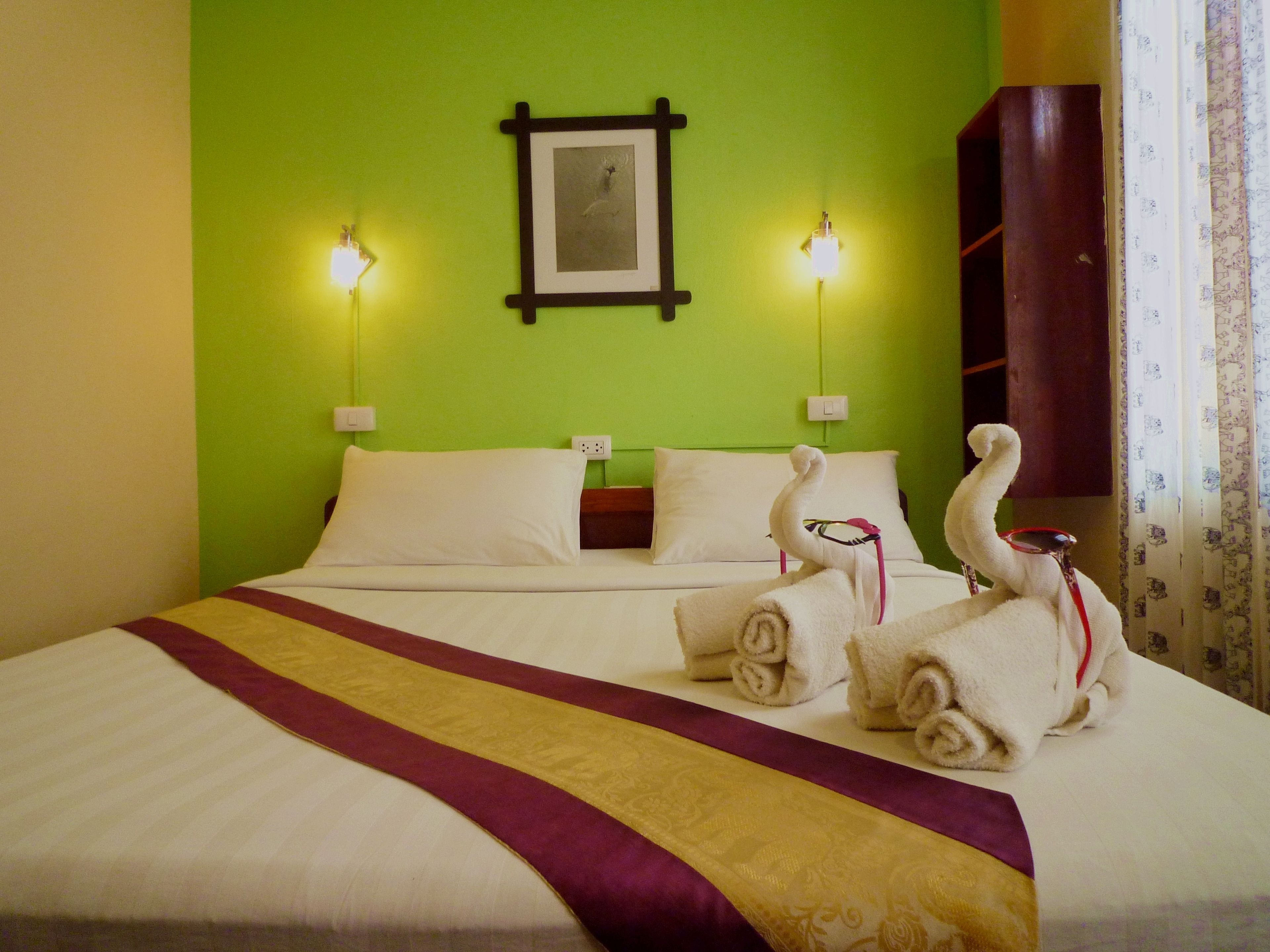 A hotel room with a green wall, a bed with white linens, two wall-mounted lamps, and a framed picture above the bed.
