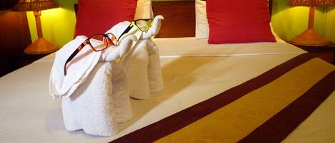 A hotel room with a neatly made bed, red pillows, and two towels with glasses on them.