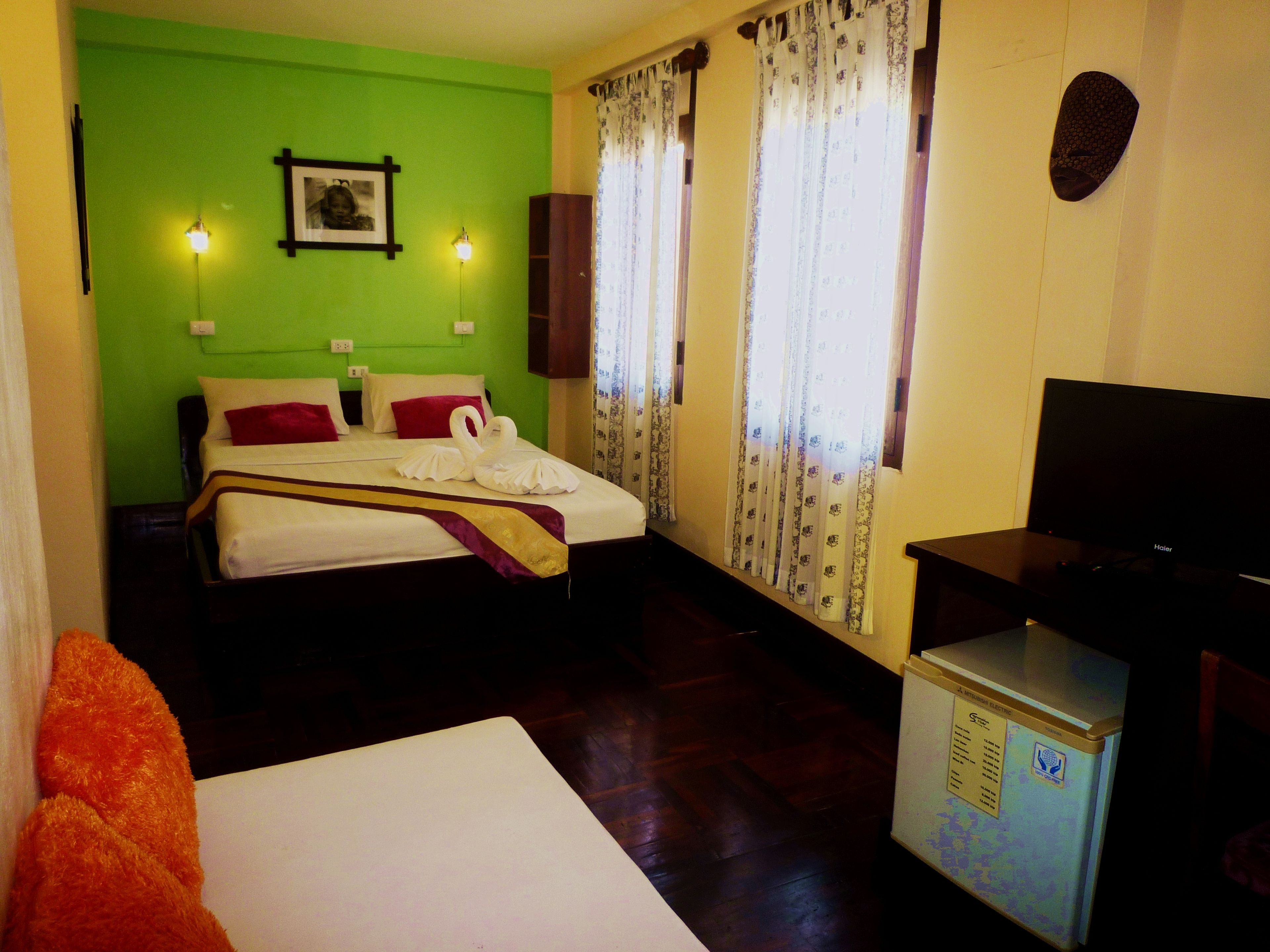 Habitación de hotel con cama, televisión, un refrigerador pequeño y una pared verde.