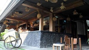 An outdoor seating area with a stone wall, wooden chairs, and a bicycle. - Omah Sinten Heritage Hotel & Resto (Surakarta)
