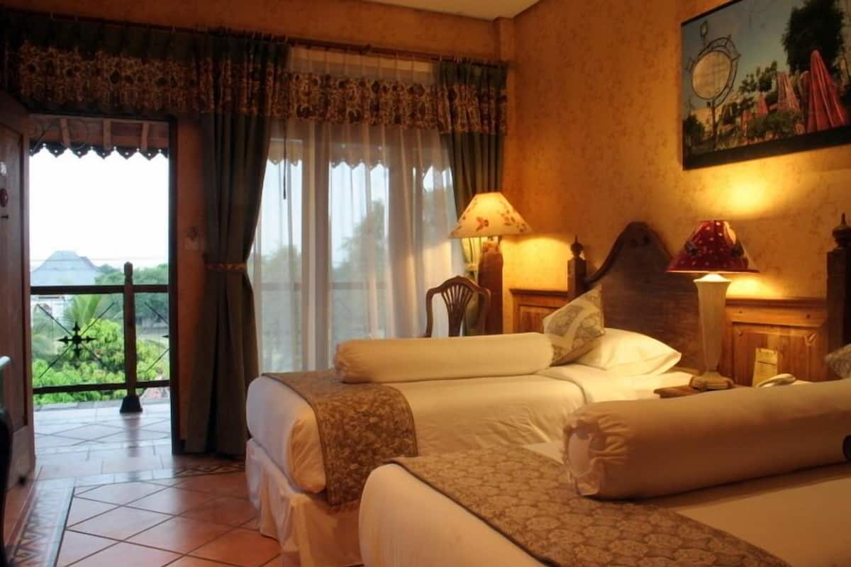 Ein Hotelzimmer mit zwei Betten, einem Fenster mit Vorhängen, einer Lampe und einem Bild an der Wand.