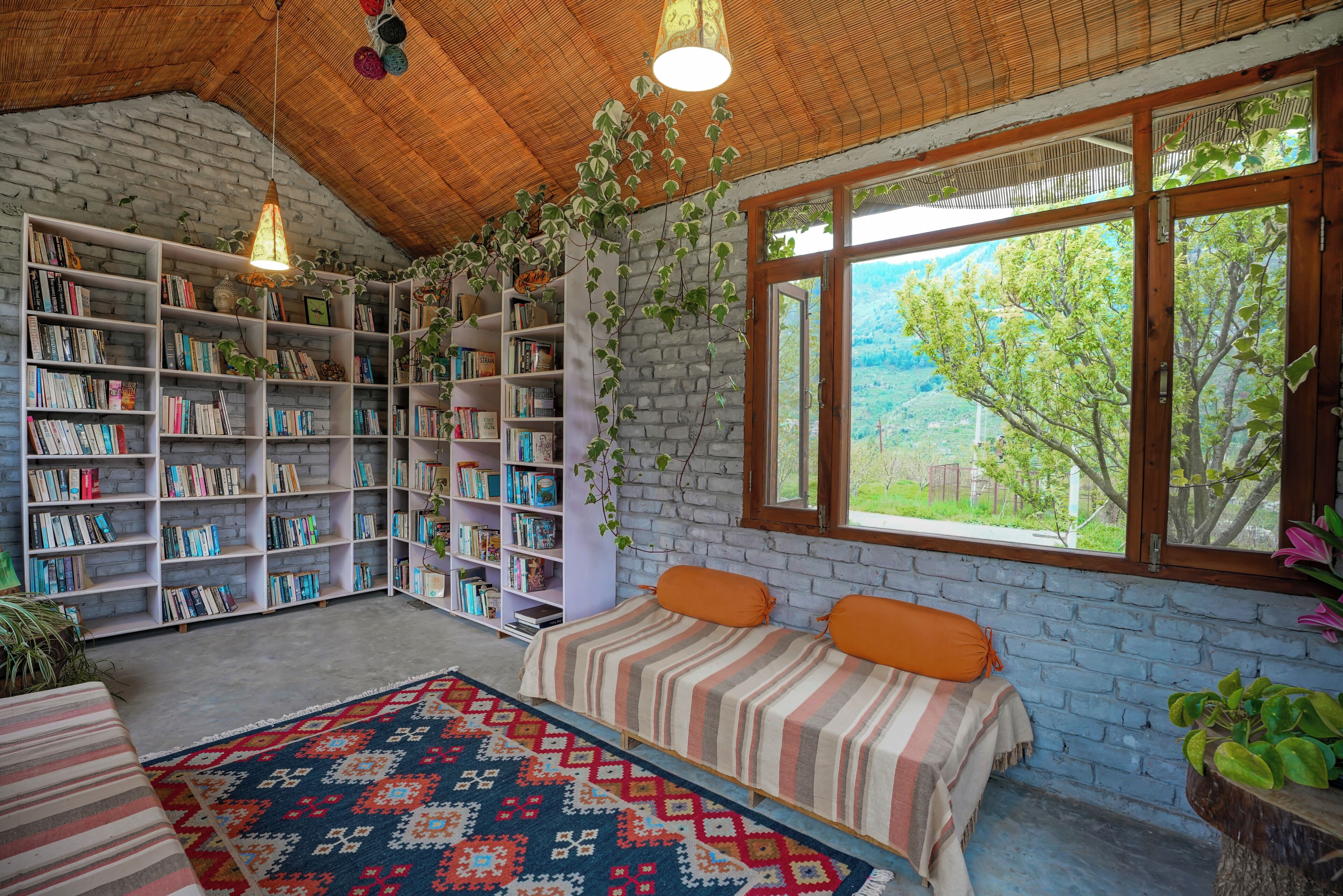 Un coin lecture chaleureux avec une grande bibliothèque, un lit confortable et une vue sur la verdure environnante.