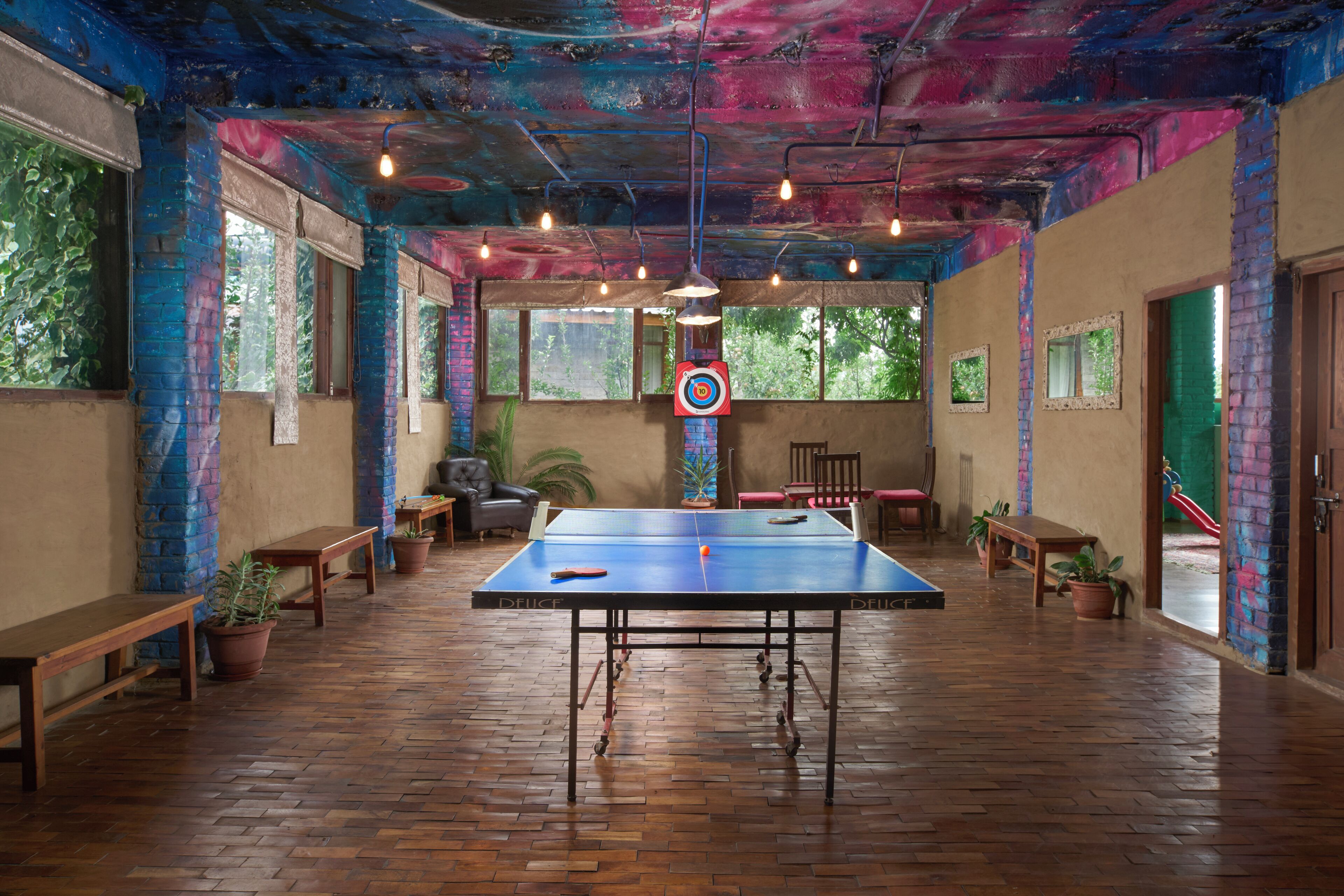 Una mesa de ping pong en una habitación con paredes de ladrillo, suelo de madera y ventanas amplias.