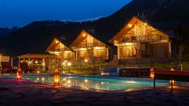 A resort with multiple wooden chalets, a swimming pool, and a mountainous backdrop. - Larisa Resort, Manali (Manali)