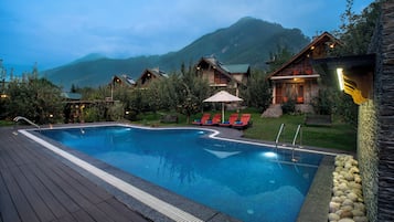Relax by the serene pool surrounded by rustic cabins with balconies and comfortable lounge seating.