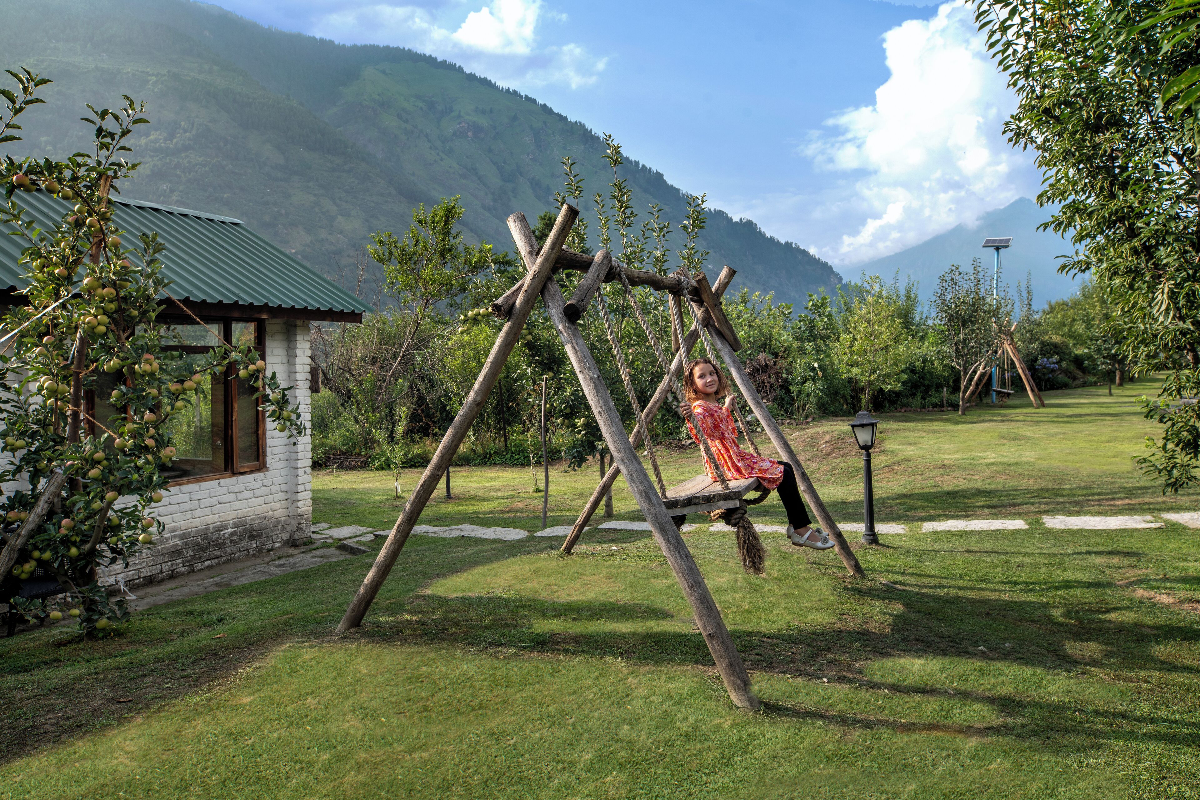 A wooden swing set in a grassy area with a small building and mountains in the background.