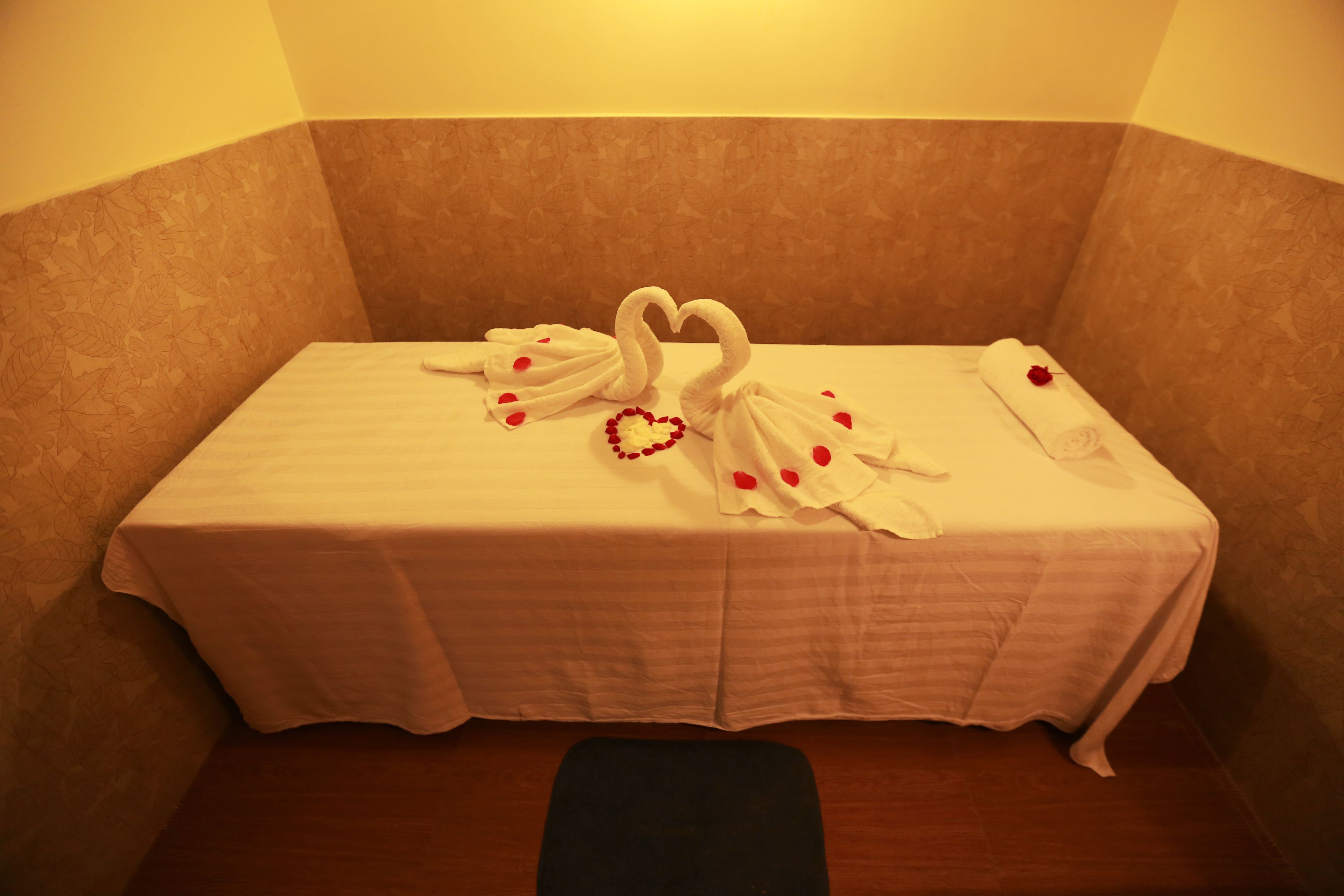 Ein Hotelzimmer mit einem mit weißer Bettdecke bezogenen Bett, einer herzförmigen Handtuchgestaltung und einer einzelnen Rose auf dem Bett.