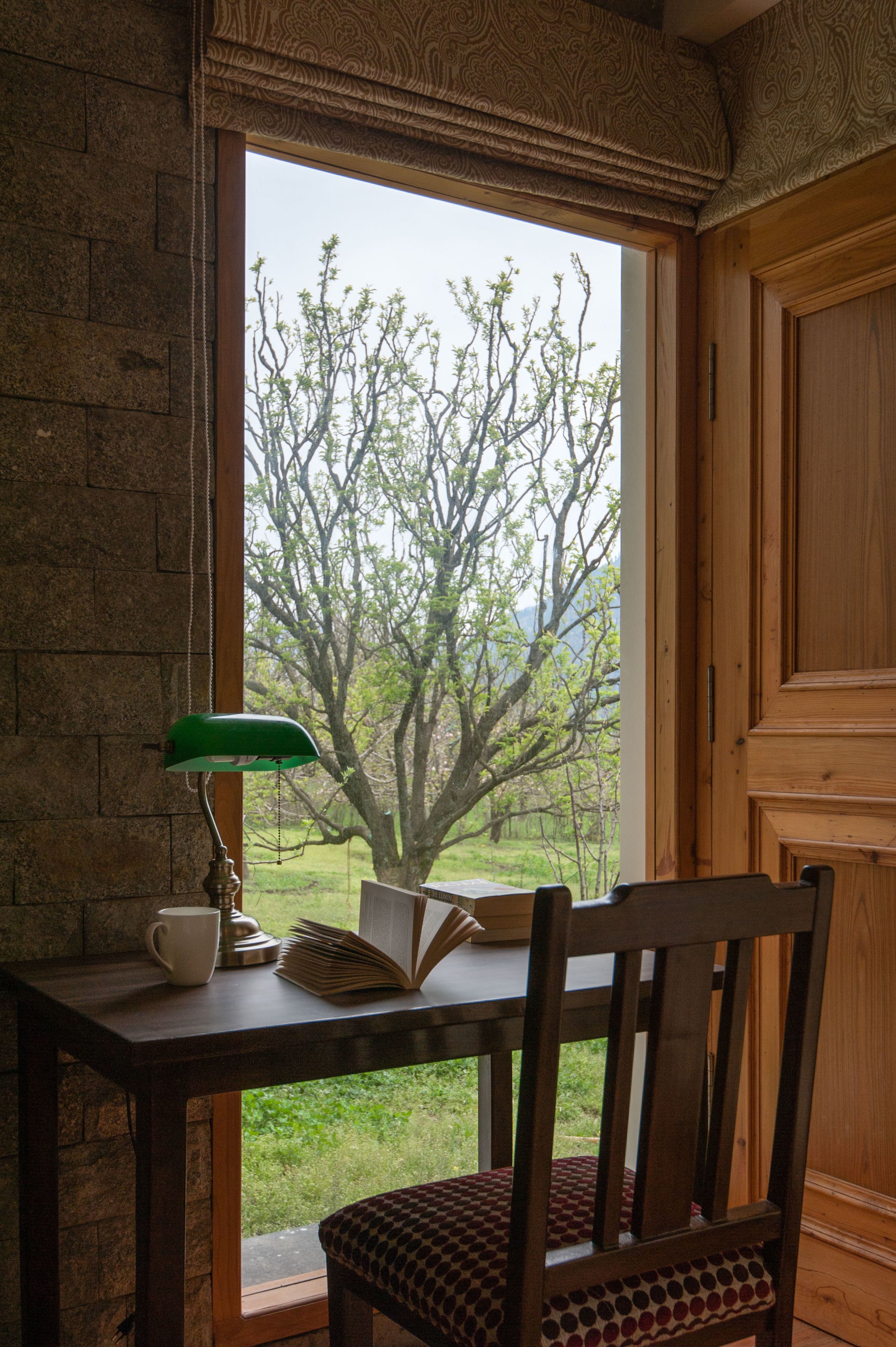 A wooden desk with a lamp, a book, and a mug. A chair is positioned in front of the desk.