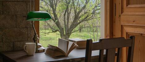 A wooden desk with a lamp, a book, and a mug. A chair is positioned in front of the desk.