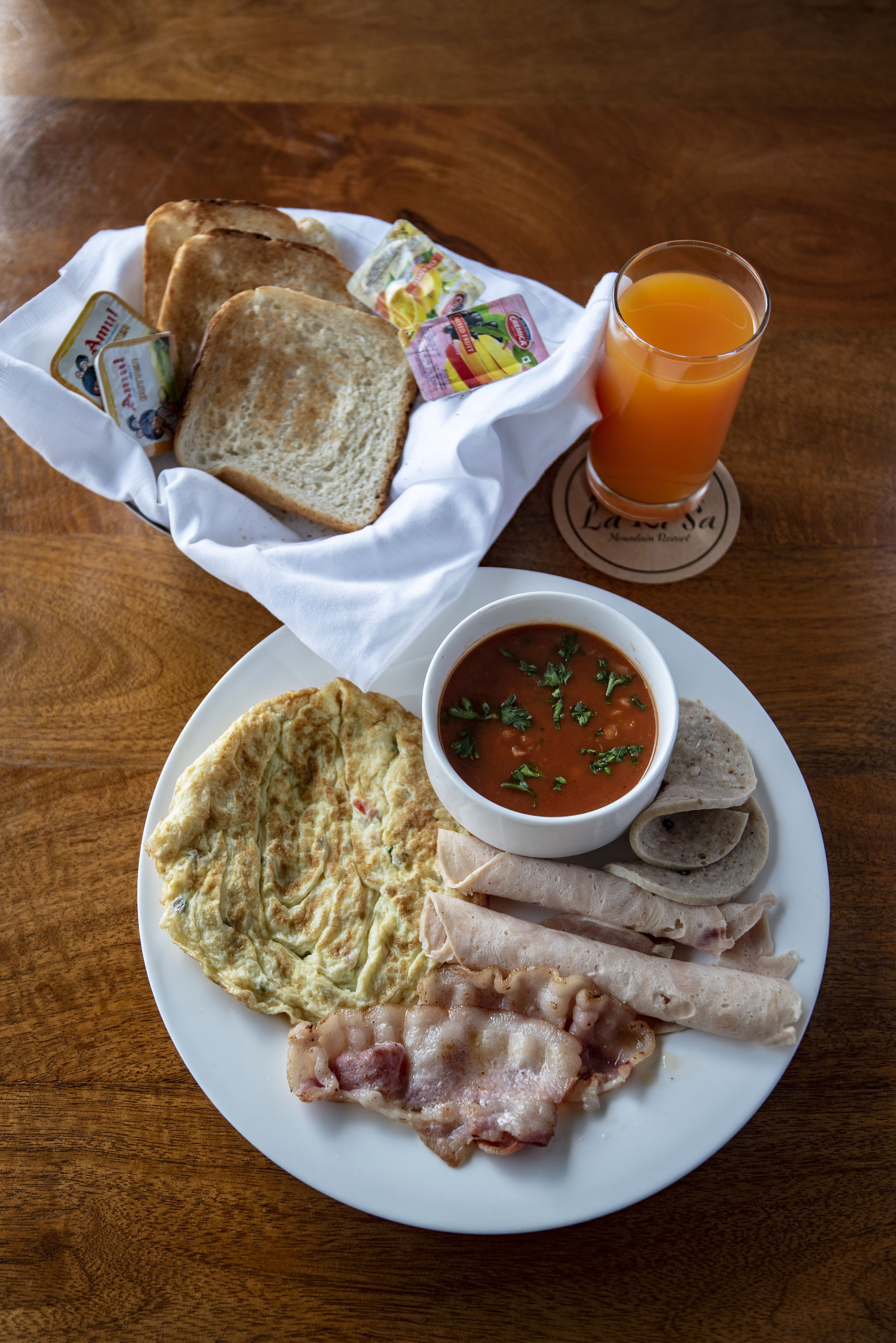 Un plato de desayuno con tostadas, sopa y tocino sobre una mesa de madera.